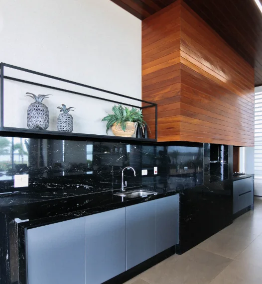 Cozinha com bancada e frontão em granito preto, armários cinza e painel de madeira no teto