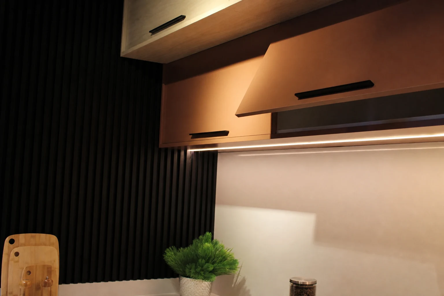 Detalhe de armários aéreos com fita de LED embutida e painel ripado preto